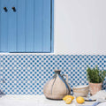 A rustic beige ceramic jug with dark blue glaze drip and handle from Merles on Papyrus on white wooden surface