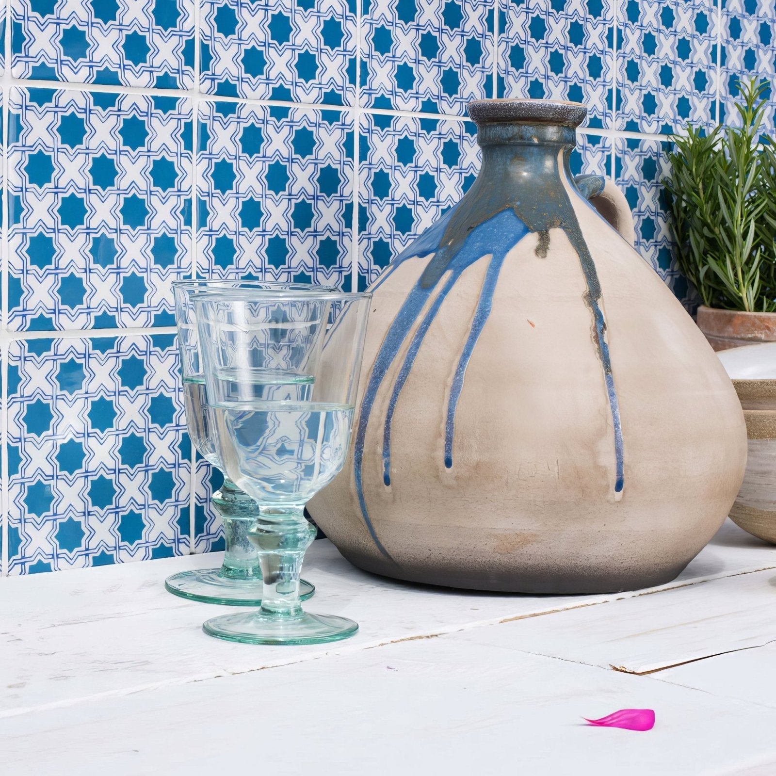 A rustic ceramic jug from merles on papyrus with a beige body, blue glaze drips, and dark gray rim and handle