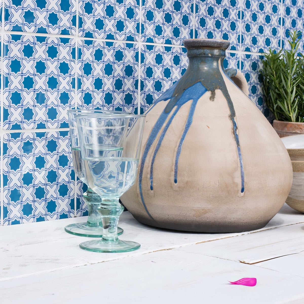 
A rustic ceramic jug from merles on papyrus with a beige body, blue glaze drips, and dark gray rim and handle
