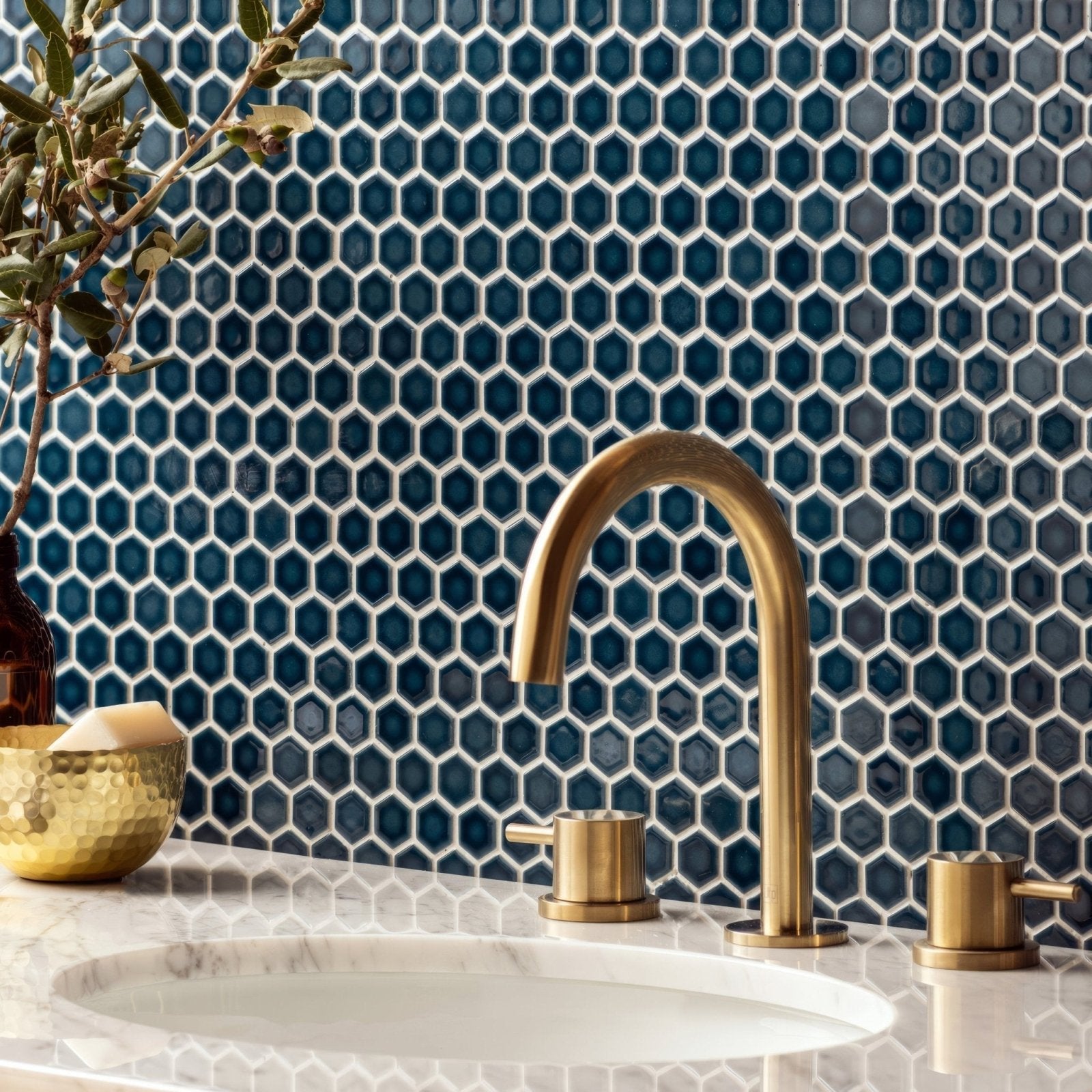 Brass-finished arched faucet with three handles against navy blue mini blue gloss hexagon mosaic tiles backdrop