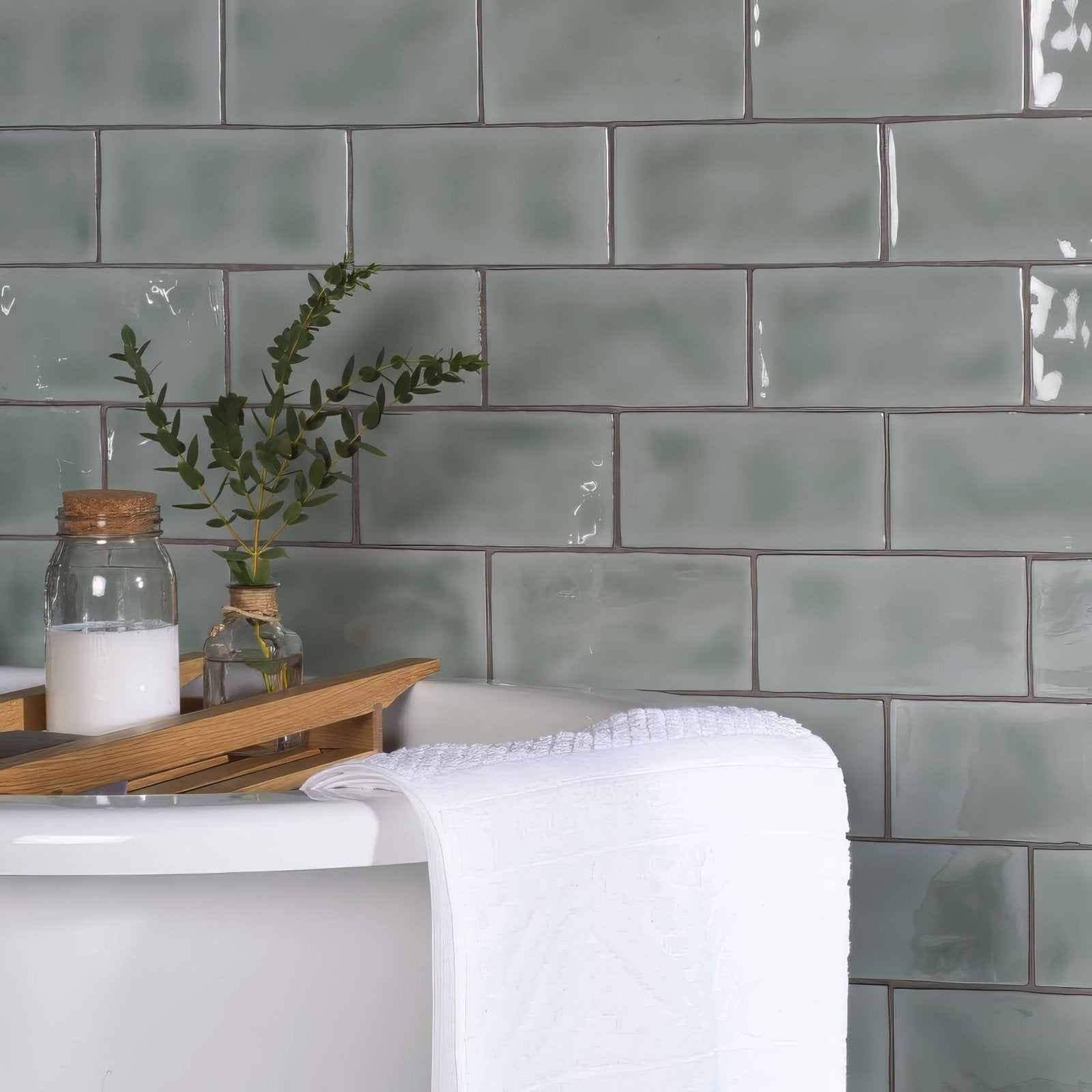 A white textured towel draped over the edge of a bathtub in a mint brick tile bathroom setting