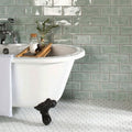 White clawfoot bathtub with black ornate feet on mint brick tile floor in a bathroom setting