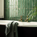 Vintage-style brass faucet set with cross handles mounted on white clawfoot bathtub against glossy montblanc emerald tiles