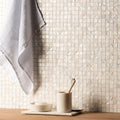 The wall covered in shimmering off-white mother of pearl white square mosaic tiles with an iridescent sheen