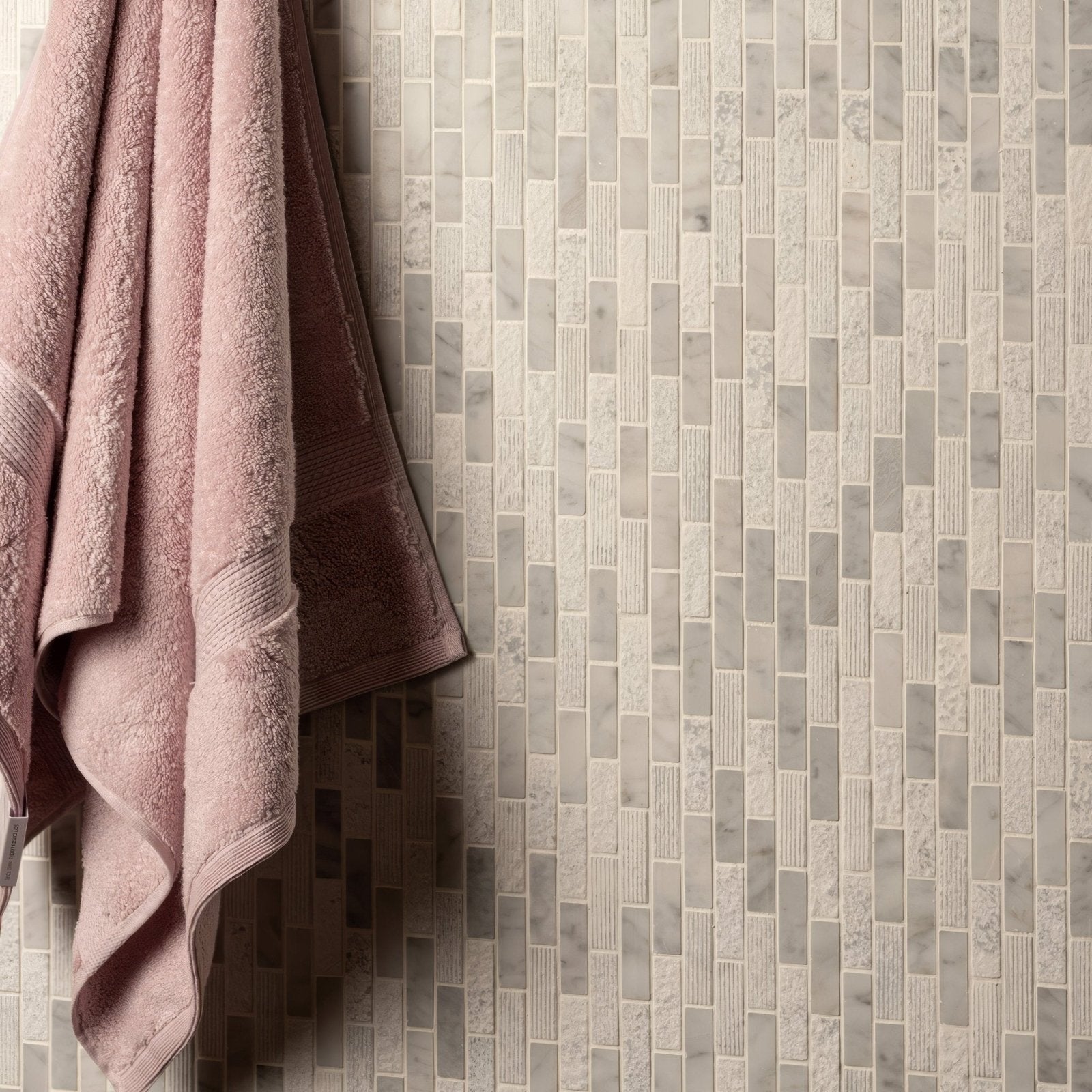 A soft pink plush towel with textured weave hanging against a nares brickbond marble mosaic tile backdrop