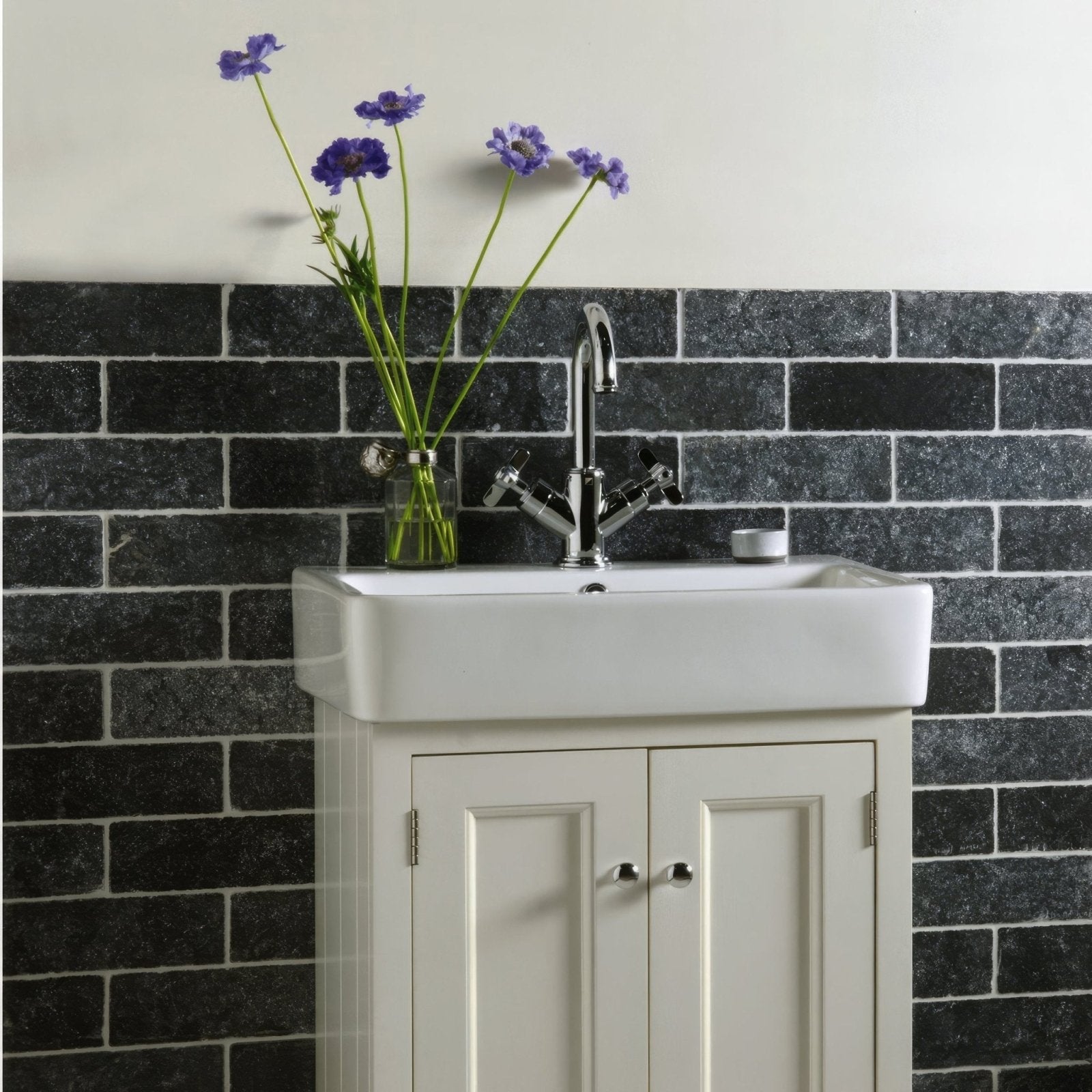 White ceramic sink with chrome faucet and matching cabinet below installed with negra black tumbled marble 7.5 x 20.3cm tiles