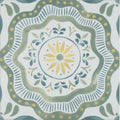 A square porcelain tile with a hand-painted floral mandala design in muted green and yellow by Nina Campbell