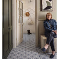 A woman in a navy blue turtleneck sits on a striped upholstered stool next to Nina Campbell La Moulade indigo porcelain tile