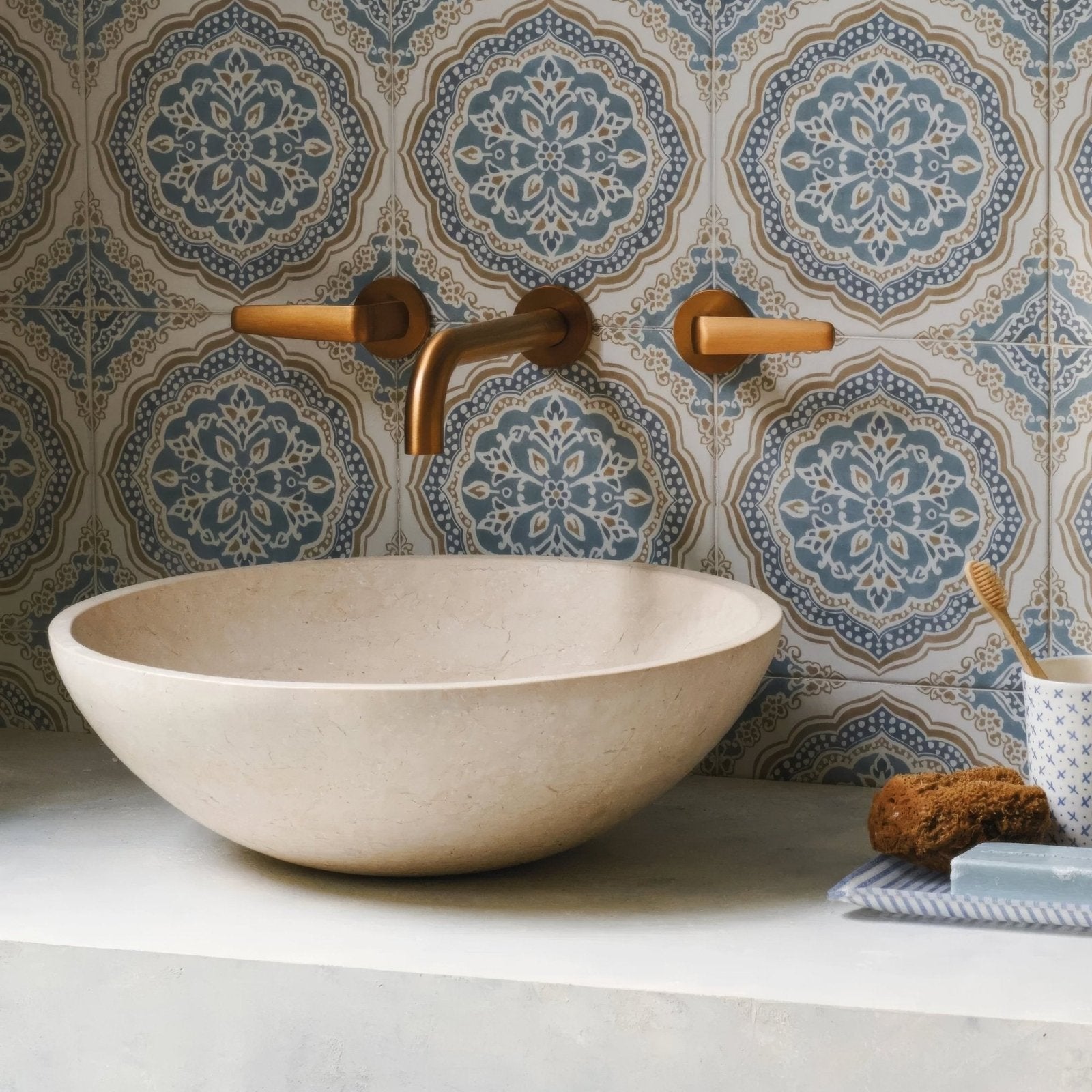 Cream-colored stone vessel sink with smooth rounded bowl shape paired with Nina Campbell Udaipur Blue porcelain tile