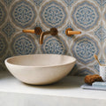 Cream-colored stone vessel sink with smooth rounded bowl shape paired with Nina Campbell Udaipur Blue porcelain tile
