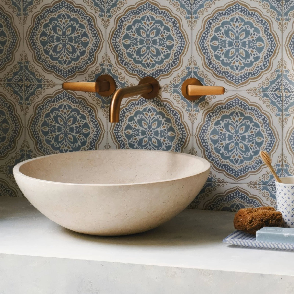Cream-colored stone vessel sink with smooth rounded bowl shape paired with Nina Campbell Udaipur Blue porcelain tile