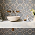 Cream-colored stone vessel sink with a smooth rounded bowl shape paired with Nina Campbell Udaipur blue porcelain tile