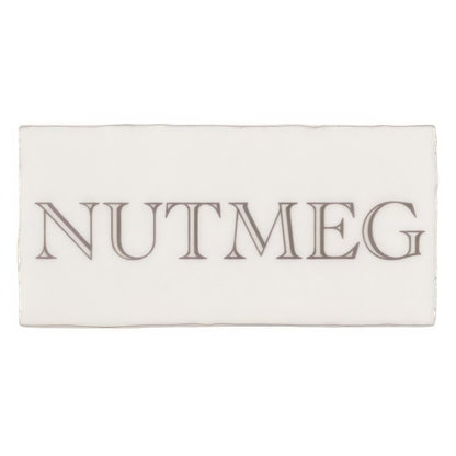 A rectangular white ceramic tile embossed with nutmeg in dark gray serif font from nutmeg in grey on cotton