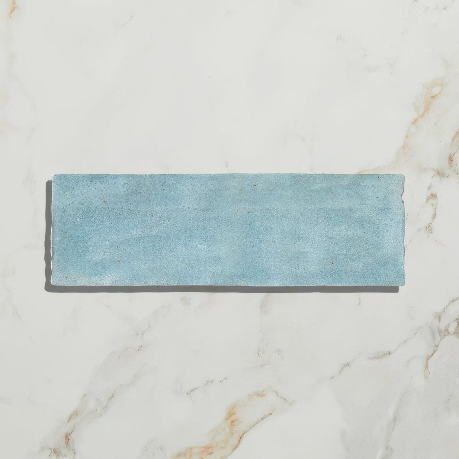A rectangular matte-finished light blue ceramic tile with subtle texture and uneven edges from oasis ceramic aqua gloss