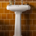 White ceramic pedestal sink with chrome faucets featured with ochre field tile background for bathroom use