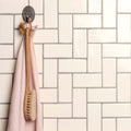 Off white half tile wooden body brush with natural bristles and soft pink towel hanging on ornate metal hook