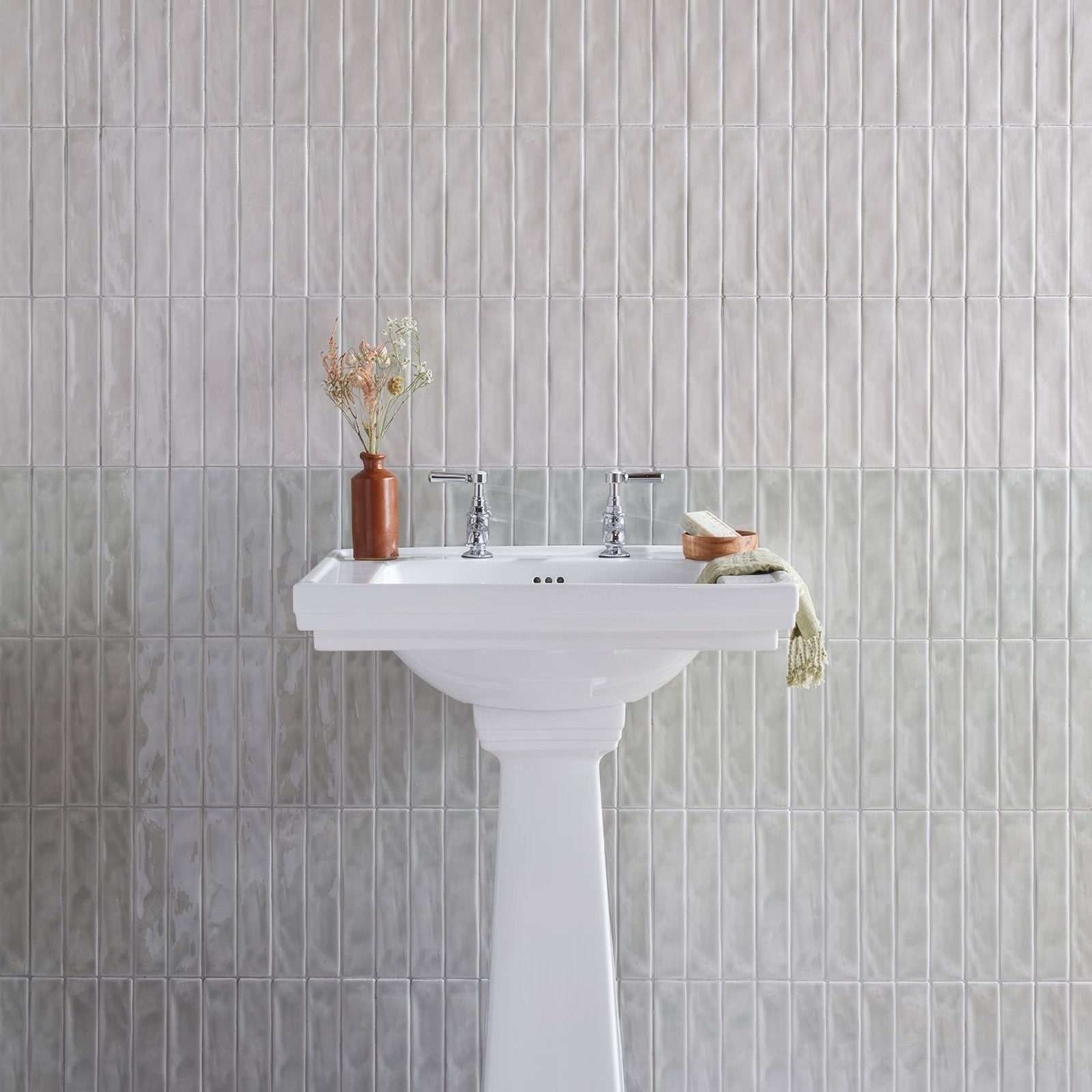 White ceramic pedestal sink with chrome faucets installed against onda chamelon wall tiles background