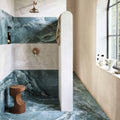 The onyx green matt marble effect tile 60 x 120 features striking teal and white marble walls and floor with a rustic wooden stool