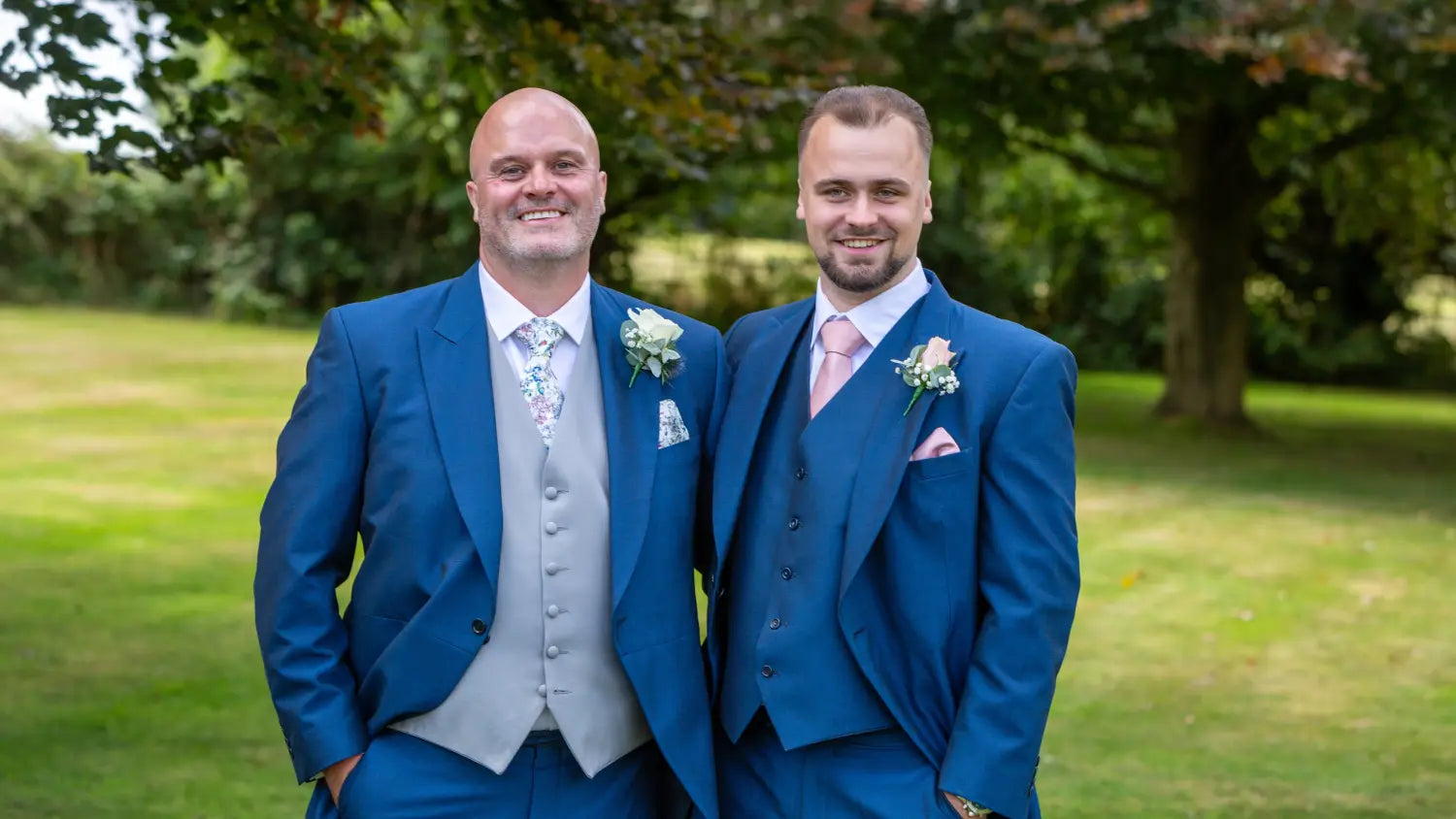 Farther and son team in blue suits standing outdoors with trees in the background
