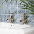Vintage-style brass-finished ormeaux red on mint bathroom taps with cross handles on a white sink and blue white tiles