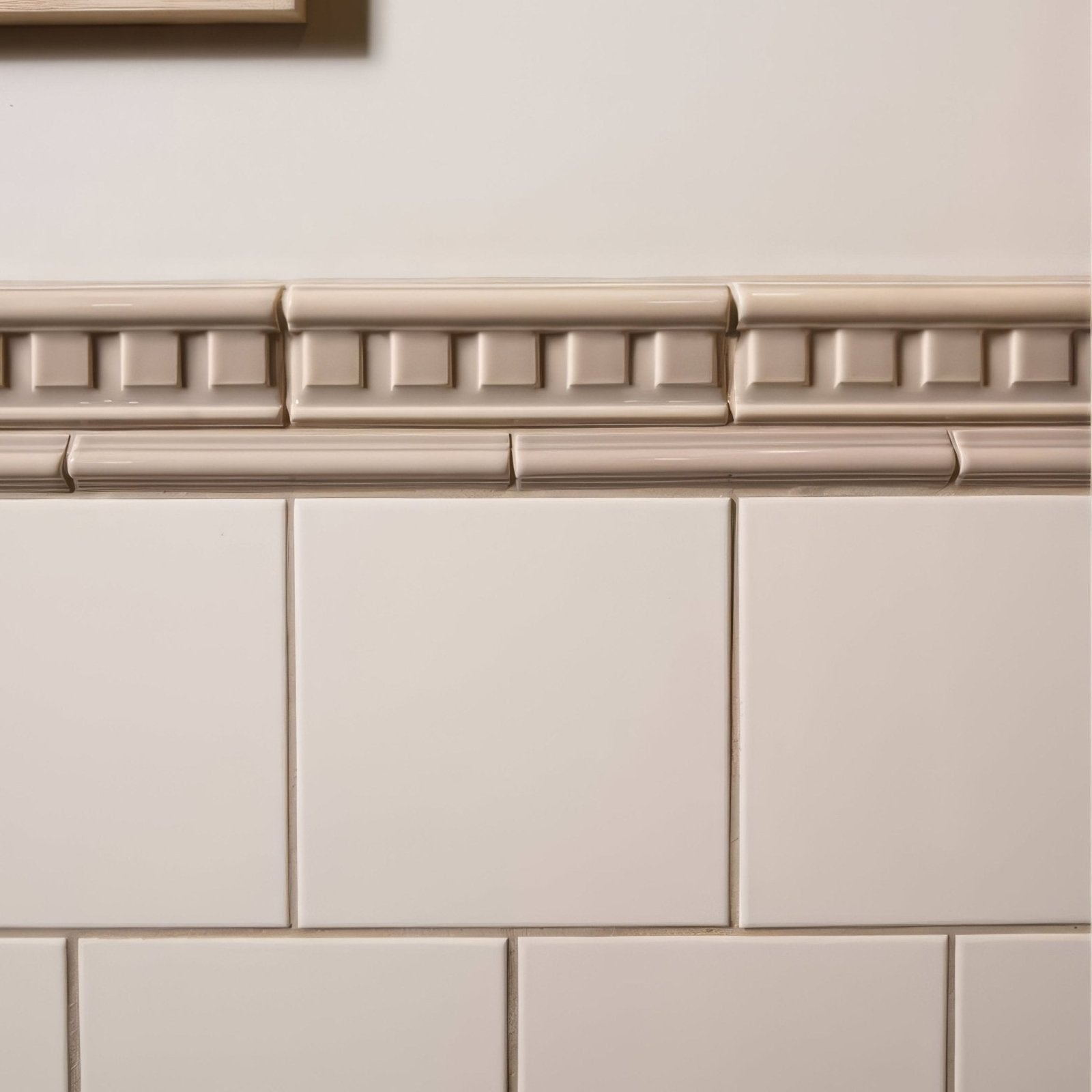 Beige ceramic palladian dentil moulding with raised rectangular border above matching square tiles