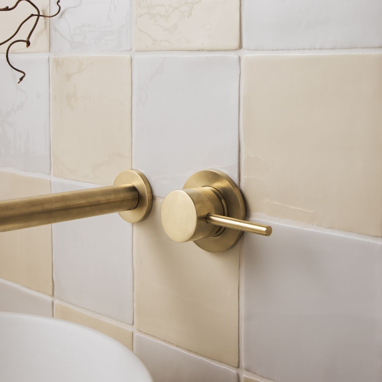 Brass-finished wall-mounted faucet with sleek cylindrical spout and circular handle in palomino field tile setting