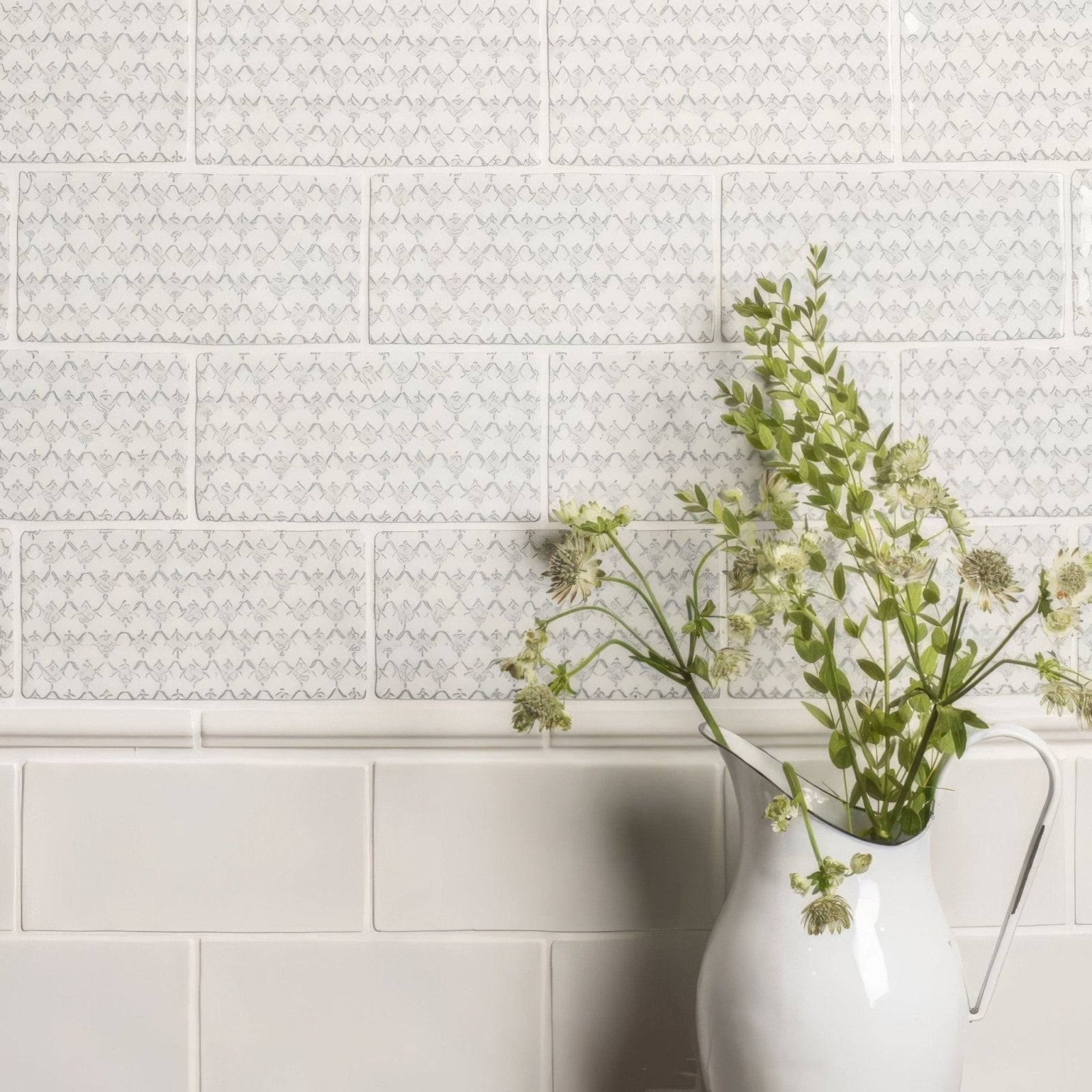 White ceramic pitcher with handle holding green flowering stems displayed with papyrus half tile wall tiles