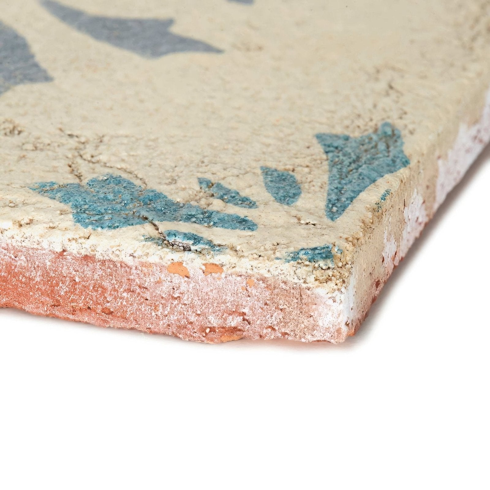 A weathered paris josette ceramic tile with a beige surface and faded blue floral patterns showing aged texture