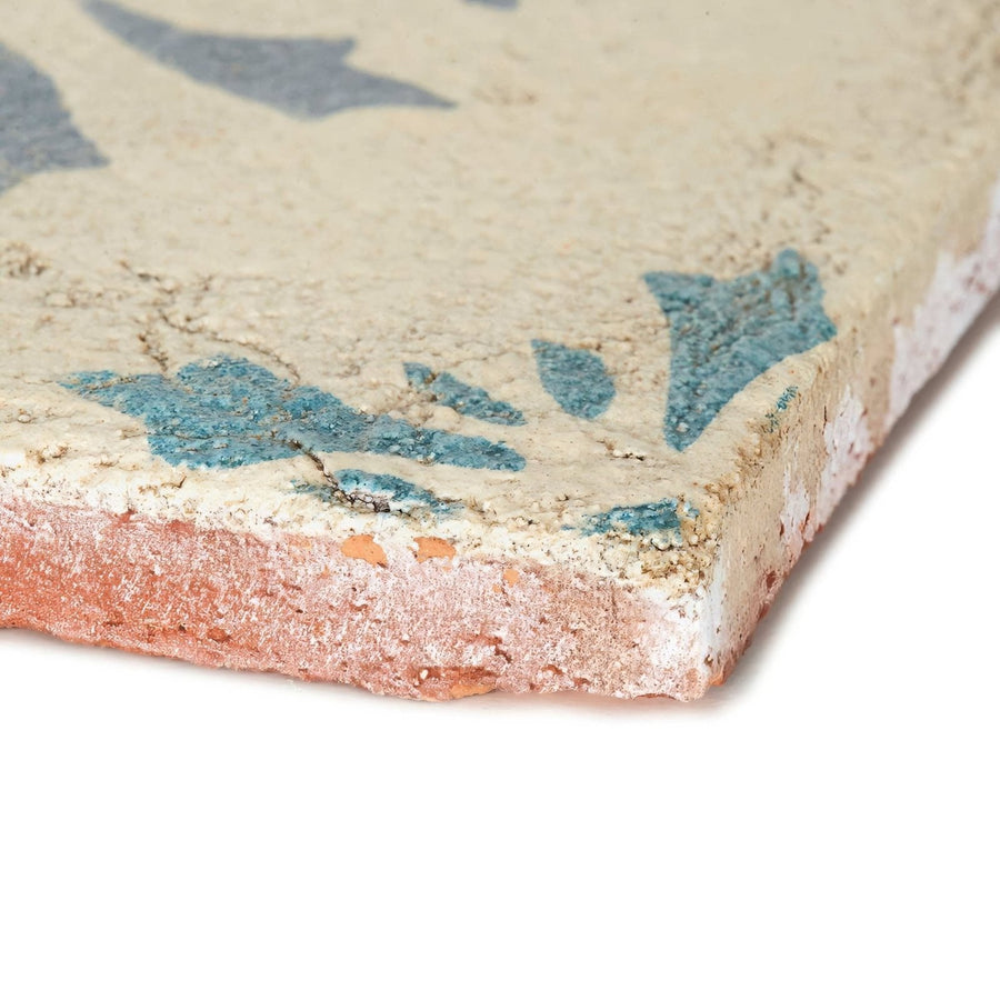 A weathered paris josette ceramic tile with a beige surface and faded blue floral patterns showing aged texture