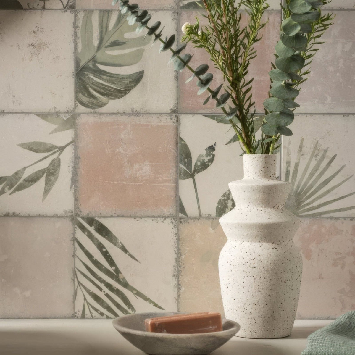 A white speckled ceramic vase with tiered organic shape holding green eucalyptus branches for patchwork botanical rose 60x30cm