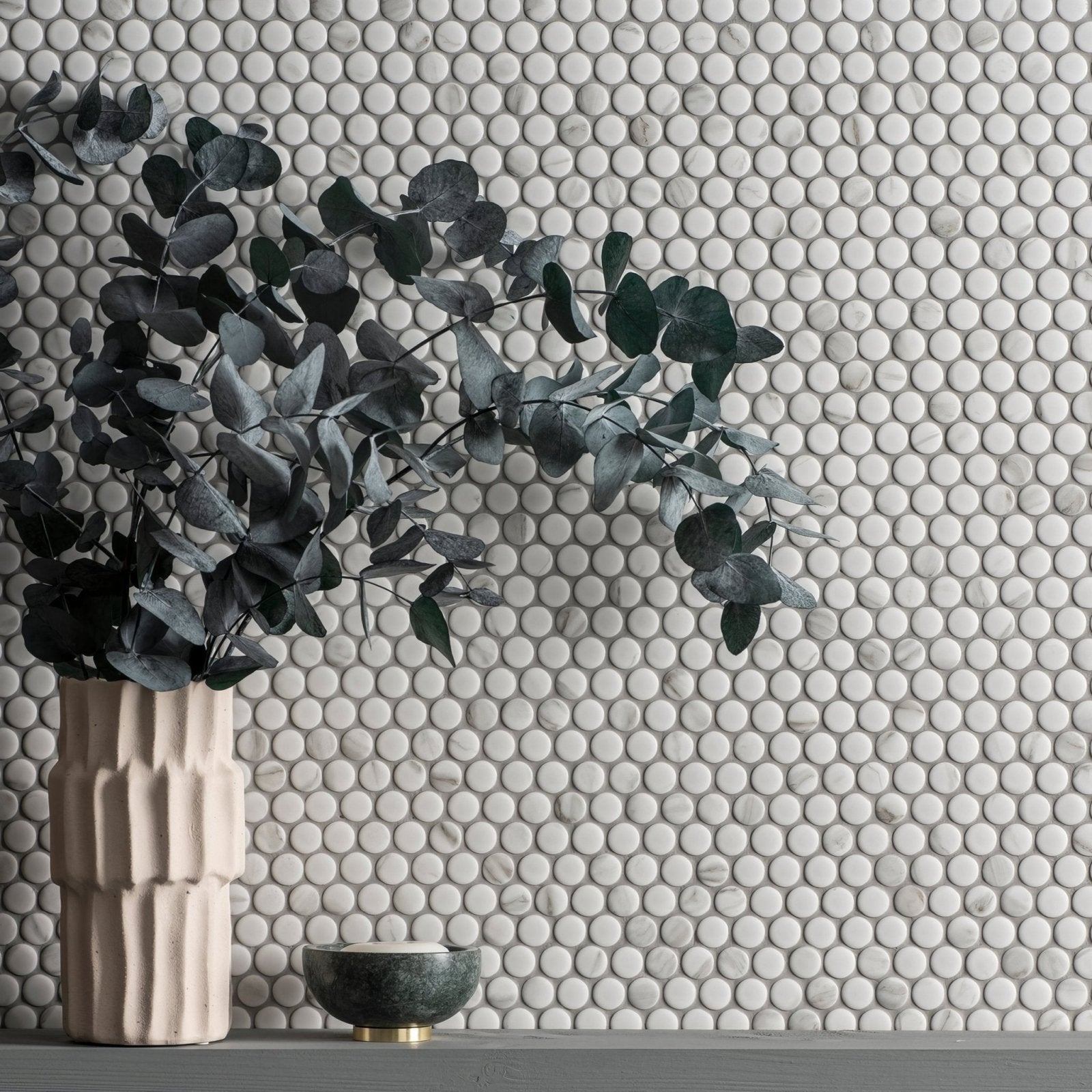 A tall beige ceramic penny round matt carrara white vase with vertical ridges holding dark green eucalyptus branches