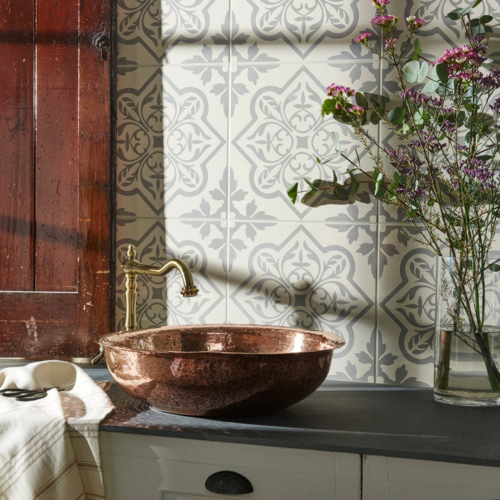 A hammered copper bowl sink with a warm reflective finish on a dark countertop in pentillie light grey on chalk