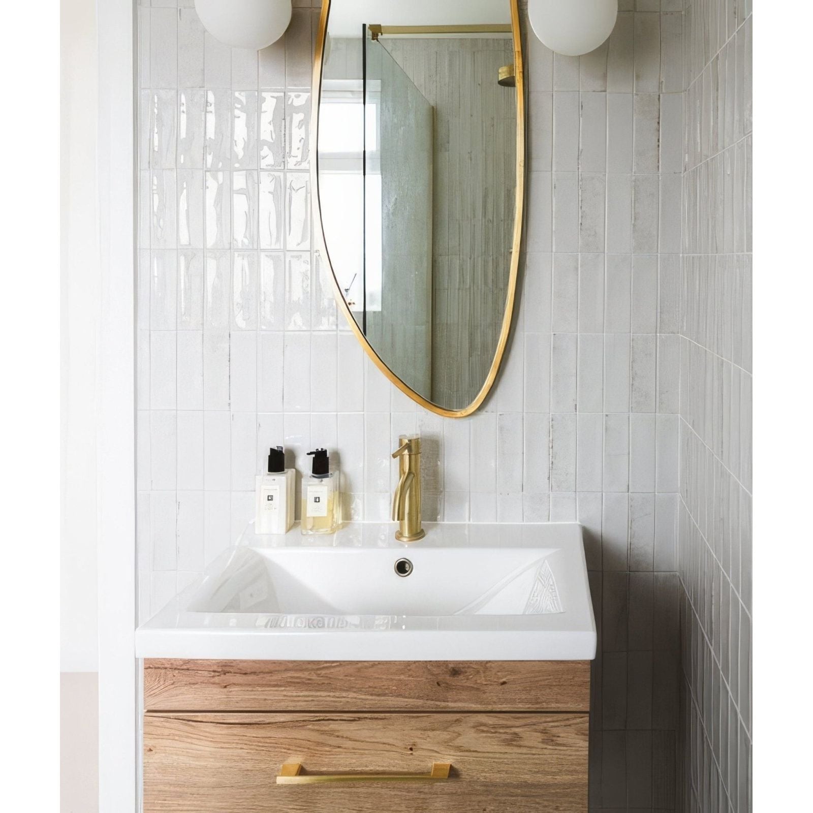 Petite porcelain gloss white sink with wooden cabinet and brass fixtures under a gold-framed oval mirror