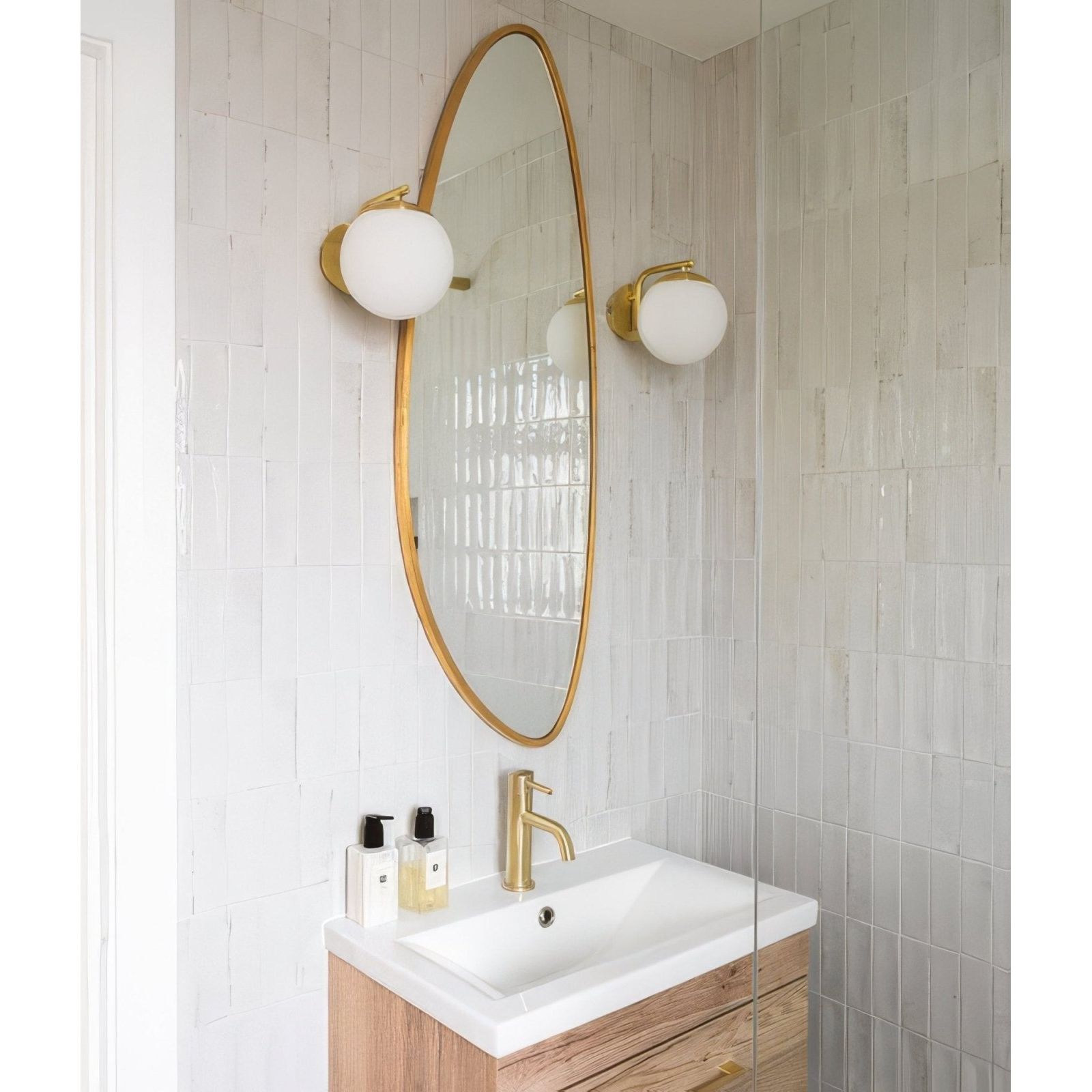 Gold-framed oval mirror with two matching petite porcelain gloss white spherical globe sconces flanking it