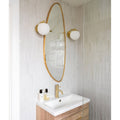 Gold-framed oval mirror with two matching petite porcelain gloss white spherical globe sconces flanking it