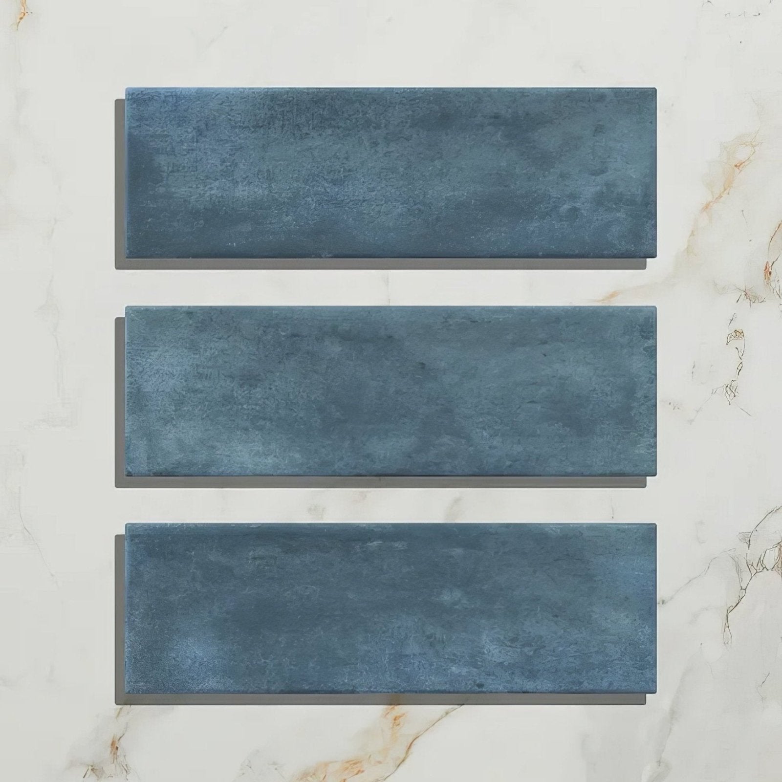 Three rectangular blue porcelain matt tiles with textured finish arranged vertically on white marble surface