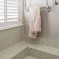 A soft blush pink Piazza Bone towel with plush texture and folded hem hangs from a chrome towel rack