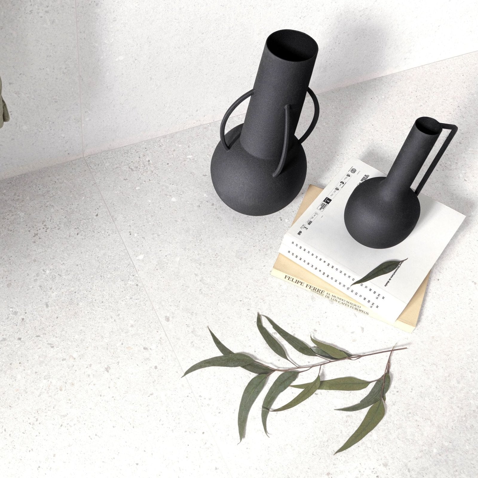Two matte black ceramic vases with minimalist sculptural handles displayed with piazza white 60 x 120cm background