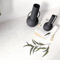 Two matte black ceramic vases with minimalist sculptural handles displayed with piazza white 60 x 120cm background