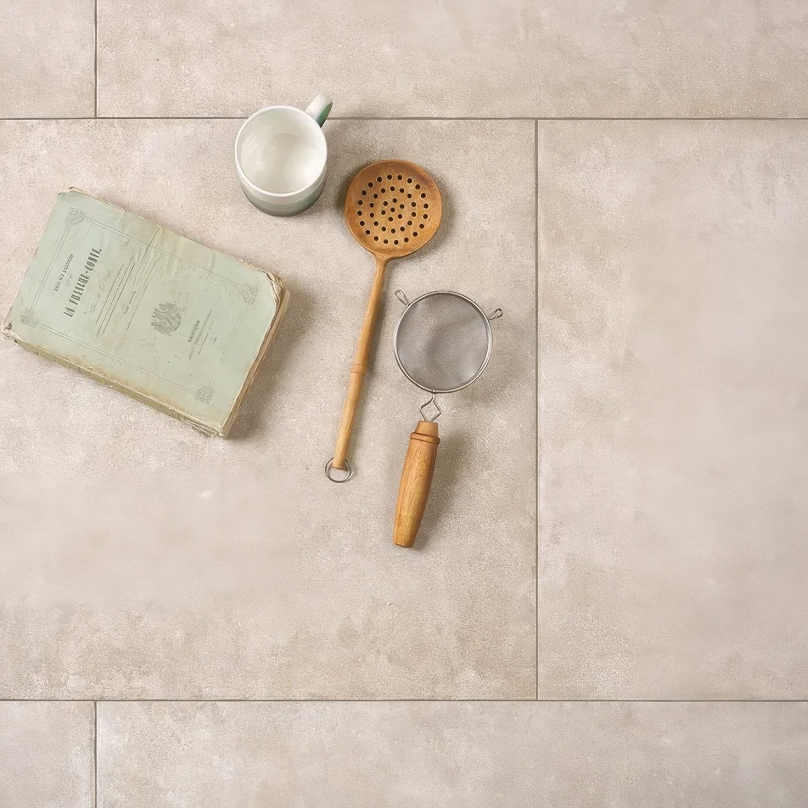 Wooden spoon with perforated head and smooth light brown handle resting on pierre porcelain paving beige surface