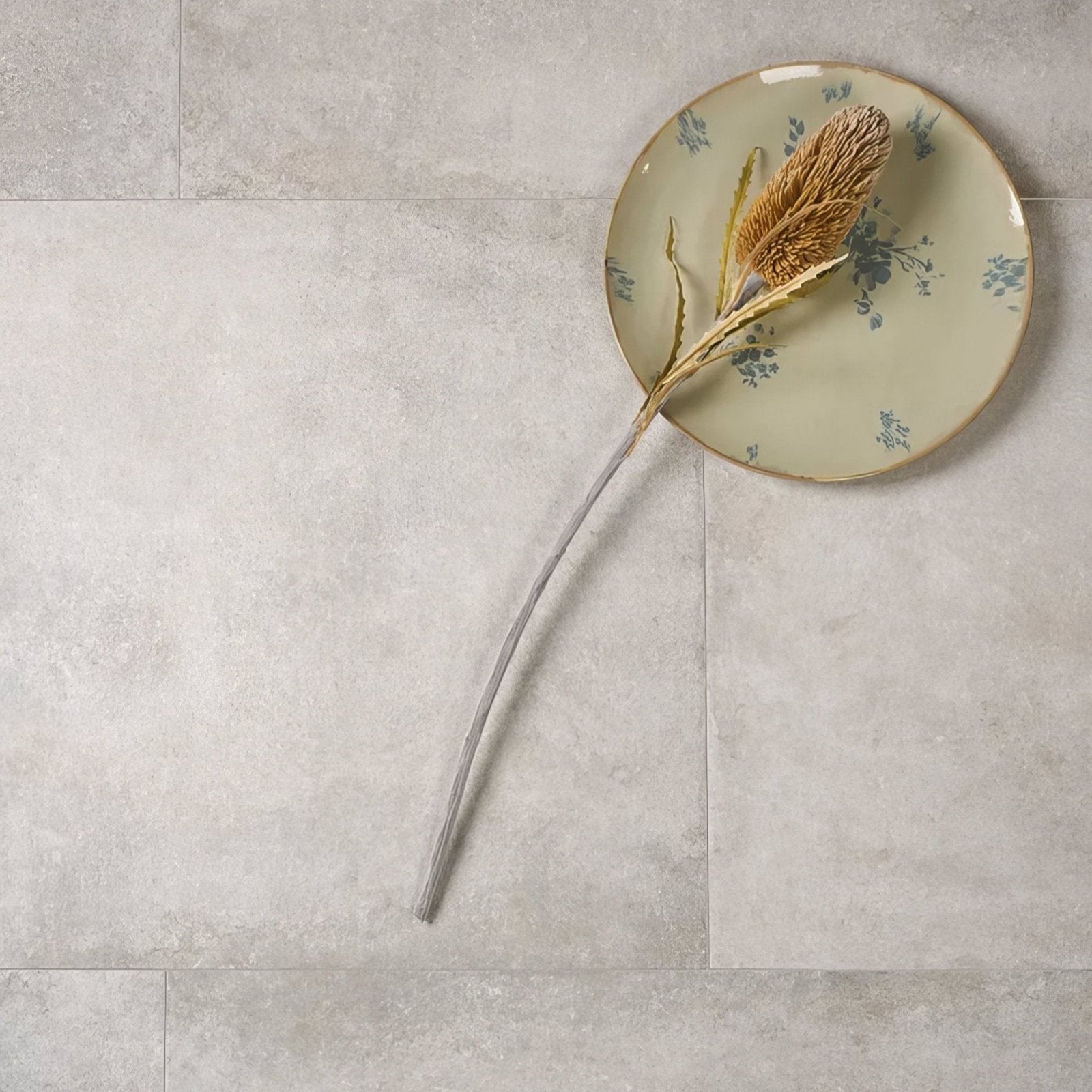 A dried goldenbrown thistle on a pale green pierre porcelain paving gris plate with blue floral patterns