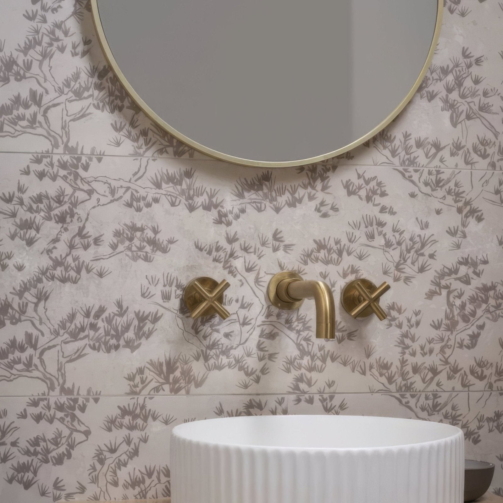 Gold-finished wall-mounted faucet with cross handles and curved spout against patterned eastern mist pine single tile wallpaper