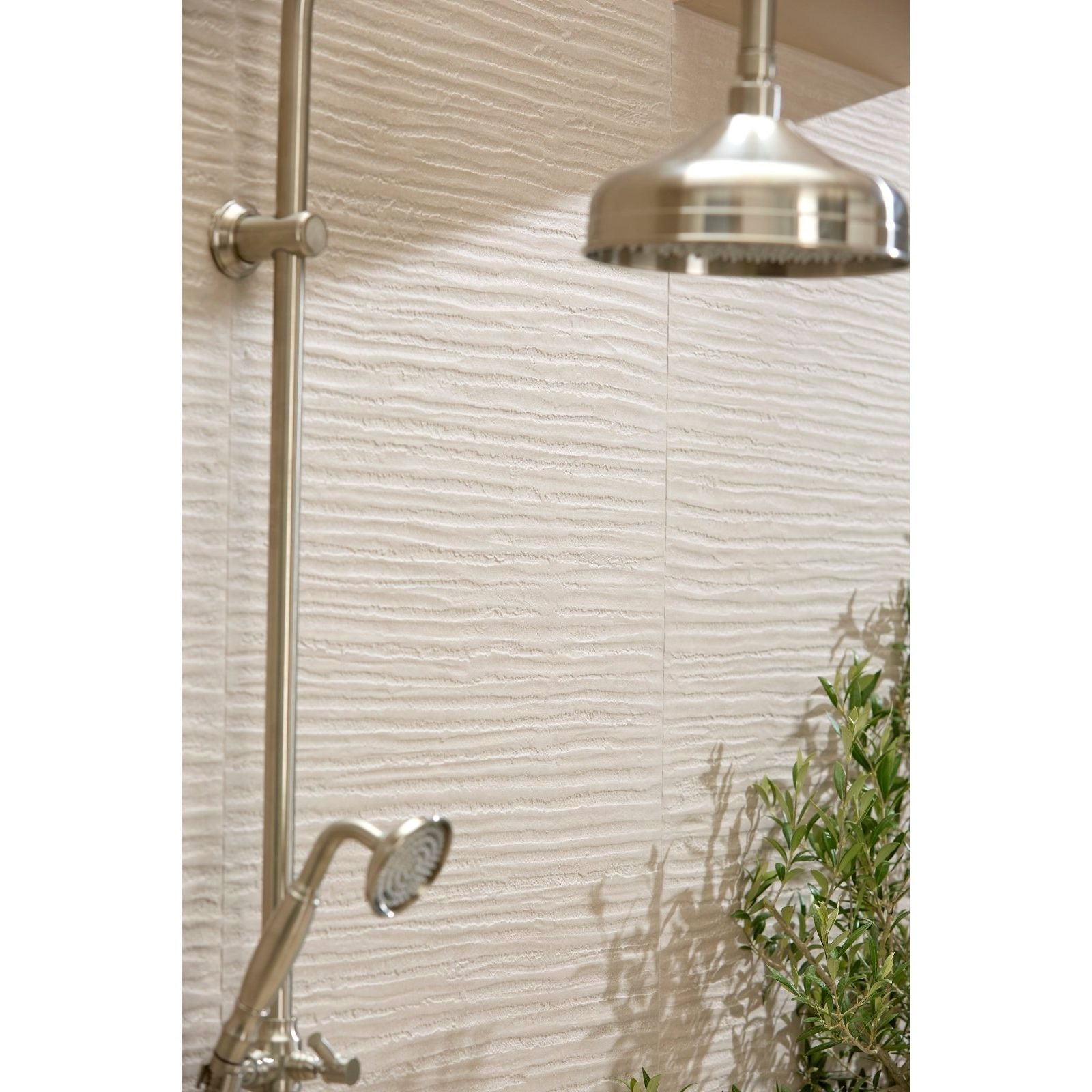 Silver-toned showerhead with sleek rounded design mounted on chrome shower arm against plastercraft linea mano porcelain mink textured tiles