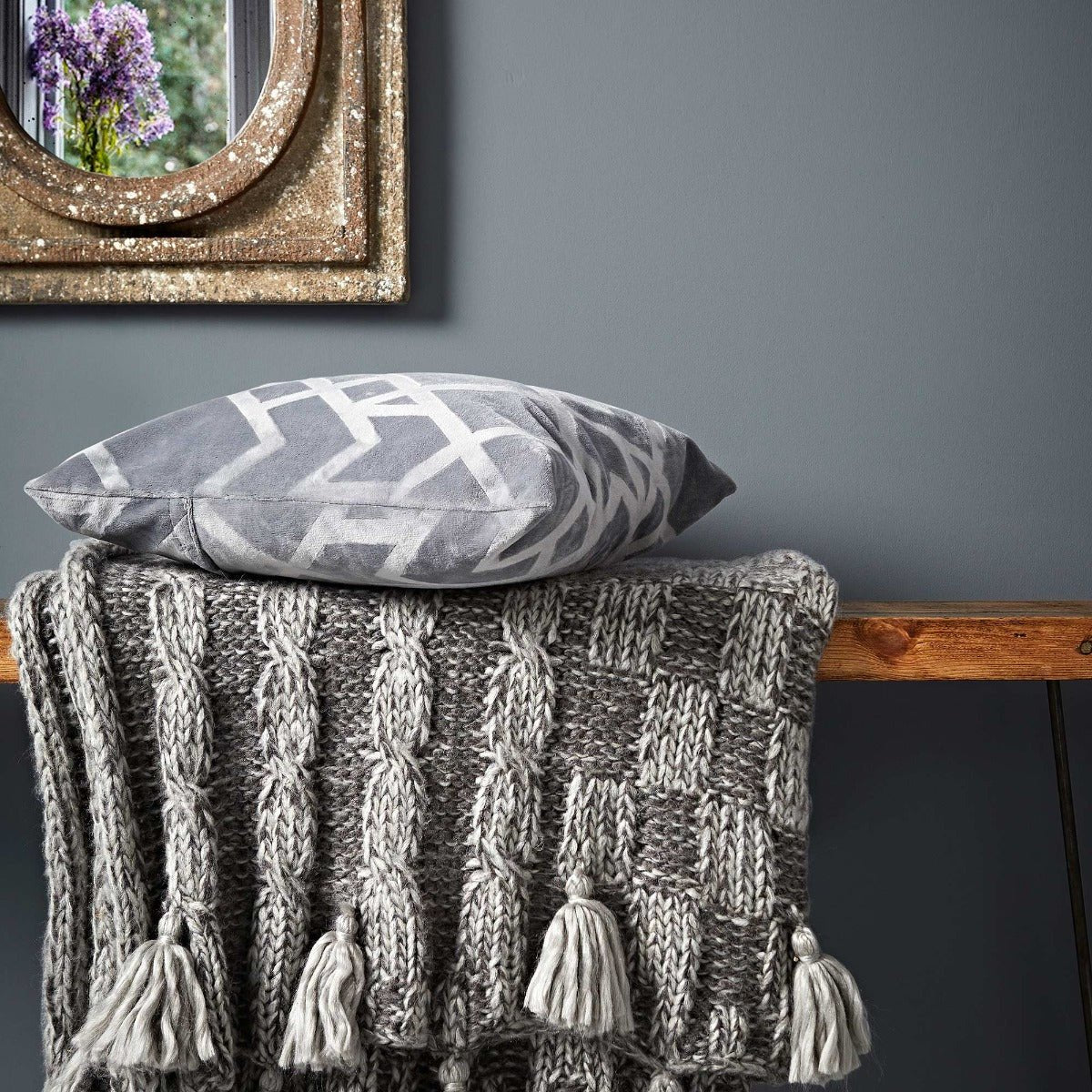 Gray plumbago cable knit throw blanket with matching tassels draped over wooden surface