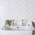 White ceramic sink with gold-finished cross-handle faucets and subtle adelfri logo paired with large brick tile porcelain