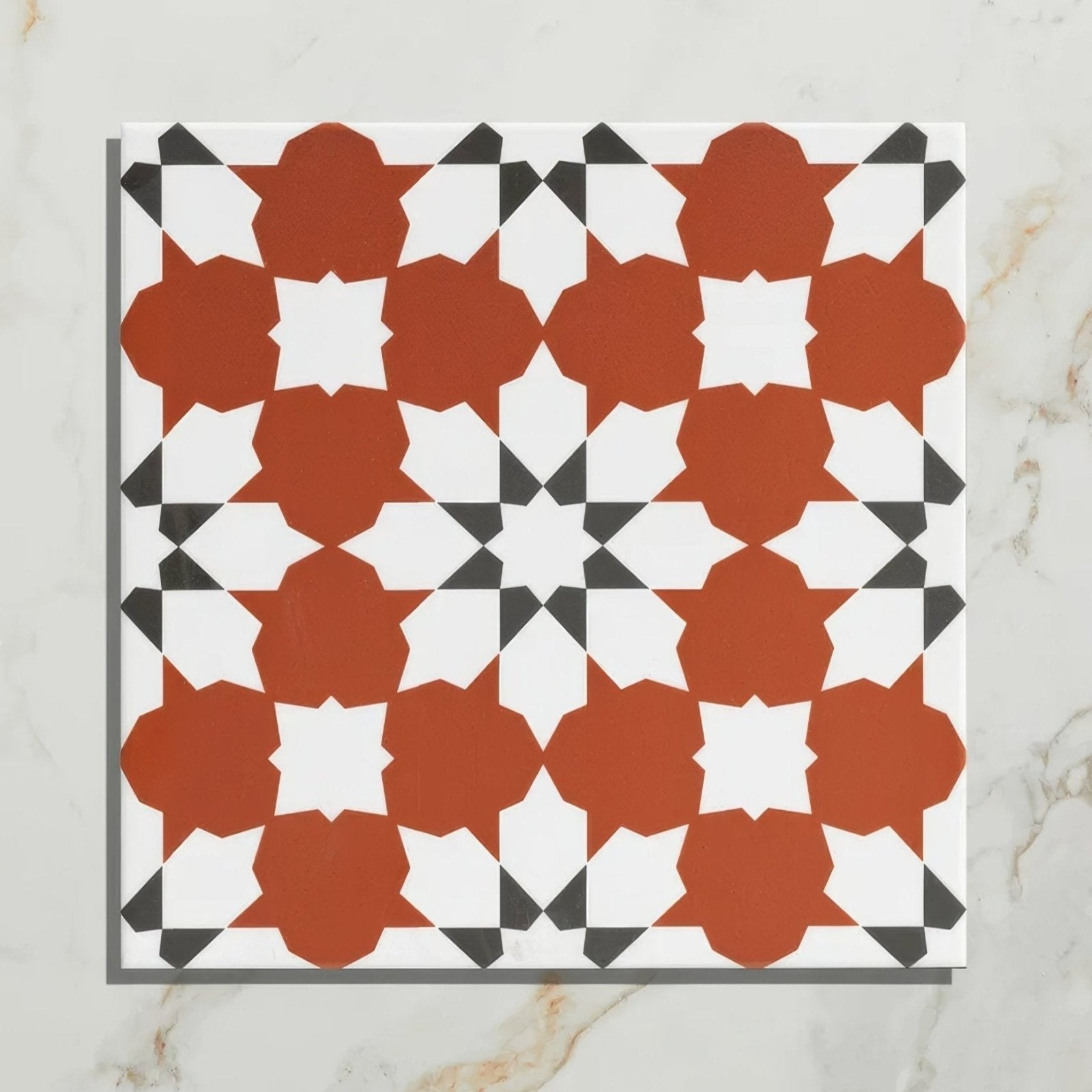 A square Belleville porcelain Vendome red tile with a rust-orange white and black geometric star pattern