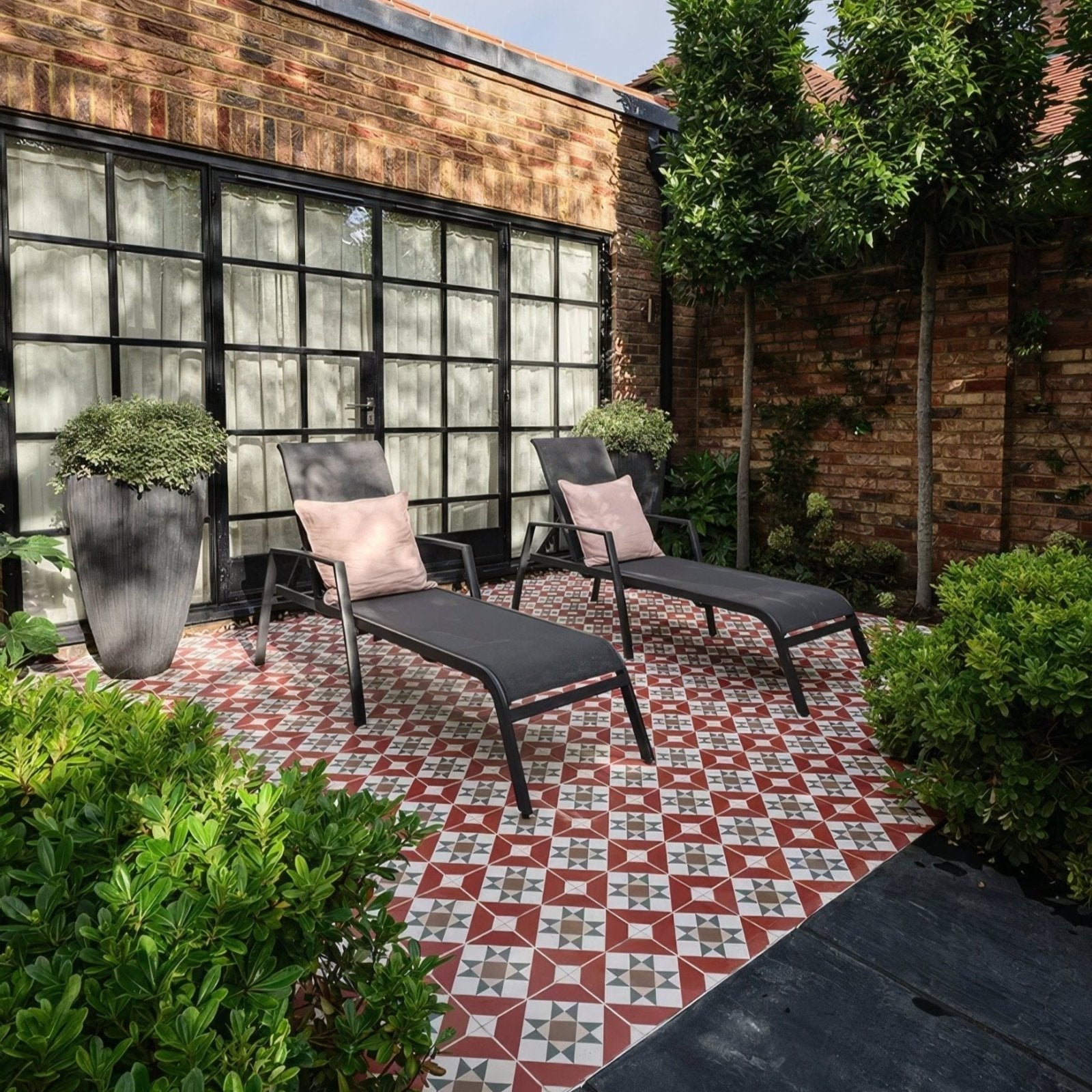 Black metal-framed brompton porcelain clarence lounge chairs with dark gray fabric cushions and light pink throw pillows