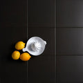 White ceramic lemon squeezer with star-shaped reamer and handle beside three yellow lemons on dark tiles brompton porcelain field liquorice