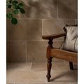 Warm-toned buscot blend limestone tumbled finish stone tiles with subtle veining on wall and floor with dark wood chair