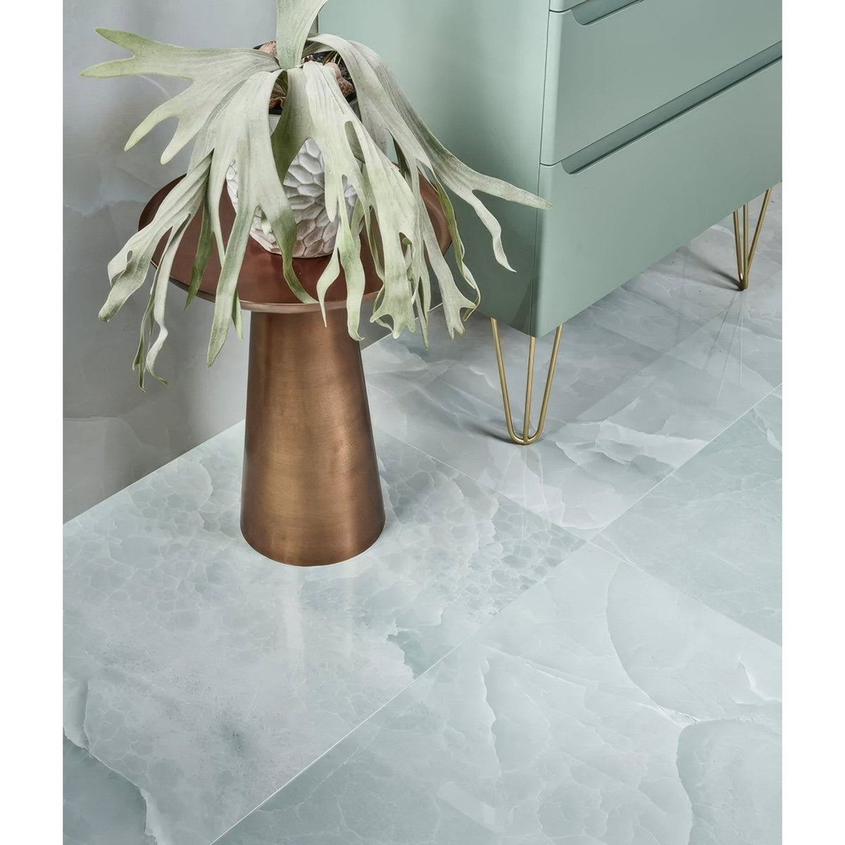 illusion Whisper Onyx Porcelain Polished Lagoon pale green marble-effect tiles with a bronze pedestal and fern